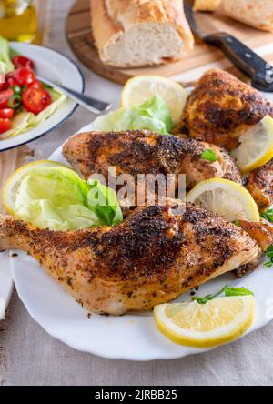 Gebackene Hähnchenschenkel mit Salat und Baguette auf einem Esstisch Stockfoto