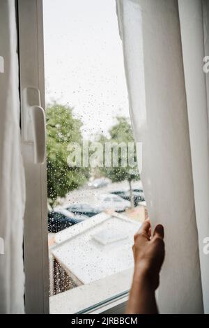 Hand einer Frau, die zu Hause Vorhang am Fenster hält Stockfoto