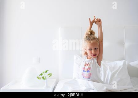 Kleines Mädchen, das die Arme im Bett streckt Stockfoto