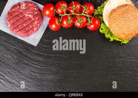 Die Zutaten für den hausgemachten Burger. Rohe Dose, Tomaten, Käse, Salat, Weizenbrötchen auf schwarzem Schieferhintergrund auf der rechten Seite mit Copy Spa Stockfoto