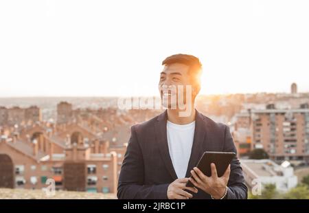 Glücklicher junger Geschäftsmann mit Tablet-PC, der vor der Stadt steht Stockfoto