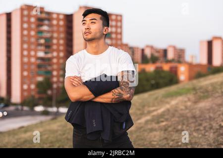 Nachdenklicher junger Mann mit den Armen, der auf einem Hügel steht Stockfoto