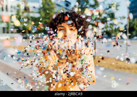 Junge Frau bläst Konfetti aus den Händen Stockfoto