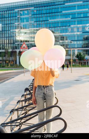 Frau, die das Gesicht mit Ballons bedeckt, die an der Fahrradparkstation stehen Stockfoto