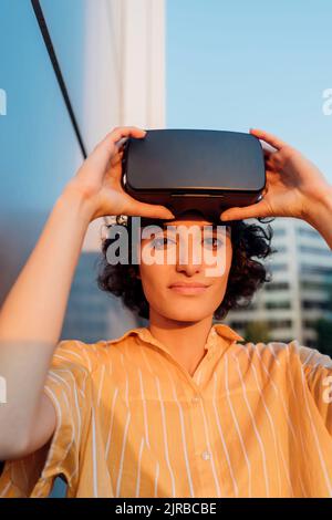 Junge Frau hält ein Virtual-Reality-Headset an der Wand Stockfoto