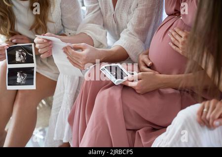 Hände einer Schwangeren mit Freunden, die das Ultraschallbild bei der Babydusche halten Stockfoto