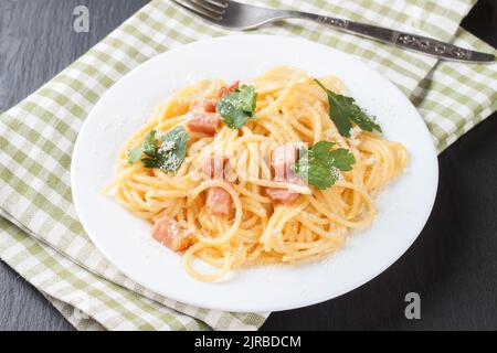 Traditionelle italienische Küche, Pasta Carbonara mit Schinken und Parmesankäse auf weißem Teller auf schwarzem Schieferhintergrund. Stockfoto