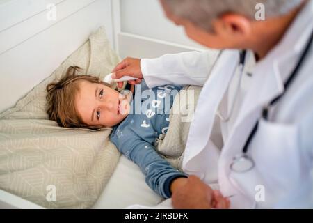 Arzt untersucht Jungen im Bett zu Hause Stockfoto