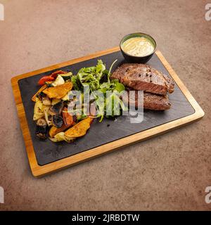 Gebratene Schweinesteaks, Koteletts, garniert mit gegrilltem Gemüse und Salat, serviert mit Senfsauce Stockfoto
