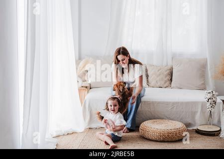 Glückliche Mutter und Tochter spielen mit Hund im Wohnzimmer zu Hause Stockfoto