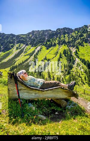 Ältere Frau auf Holzbank liegend, Berg Nebelhorn, Allgau, Bayern, Deutschland Stockfoto