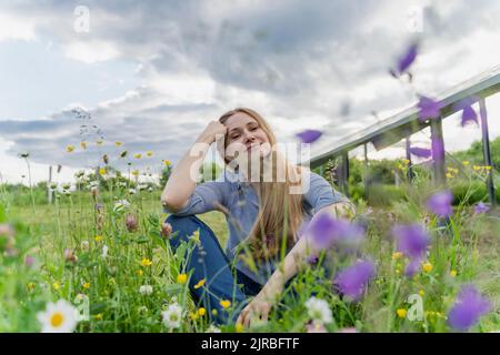 Lächelnder Ingenieur, der auf Gras vor Solarzellen sitzt Stockfoto