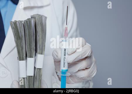 Nahaufnahme einer modernen Ärztin in weißer medizinischer Robe mit Monkeypox-Impfspritze und Geldbeutel vor grauem Hintergrund. Stockfoto