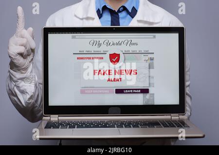 Nahaufnahme einer modernen Ärztin in weißem medizinischen Gewand, in dem ein Laptop mit gefälschter Nachrichtenwarnung von Monkeypox auf grau dargestellt wird. Stockfoto