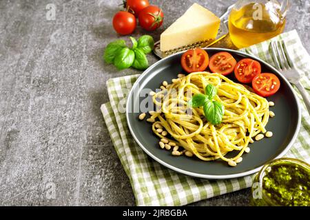 Pasta mit frischer hausgemachter Pesto-Sauce auf grauem Hintergrund mit Kopierfläche. Traditionelle italienische Spaghetti mit Lebensmitteln Zutaten Pesto Sau?e, Tomate, par Stockfoto