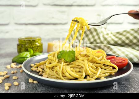 Pasta Pesto mit Gabel in dunklem Teller auf grauem Betongrund. Traditionelle italienische Spaghetti mit Zutaten für Lebensmittel Pesto-Sauce, Tomaten, Parmesan che Stockfoto