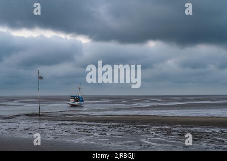 Deutschland, Schleswig-Holstein, Pellworm, Sturmwolken über Fischerboot, die bei Ebbe am Strand zurückgelassen wurden Stockfoto