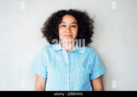 Lächelnde lockige Frau, die vor der Wand steht Stockfoto