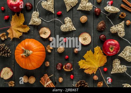 Flache Herbst- oder Herbstzusammensetzung mit Kürbis, Äpfeln, Blättern, Nüssen und Zimtstangen auf dunklem Holzhintergrund. Stockfoto