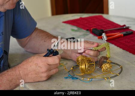 Mann, der ein handgearbeittes Schlagzeug mit verschiedenen Materialien, spezielle Zangen, mit gekonnten Händen auf einem Granittisch und einigen Gegenständen herstellt, selektiver Fokus. blurr Stockfoto