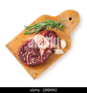 Frisches, rohes Fleischsteak mit Knochen, Gewürzen, Rosmarin, Knoblauch und Olivenöl auf Holzschneidebrett, isoliert auf weißem Hintergrund. Draufsicht. Flach l Stockfoto