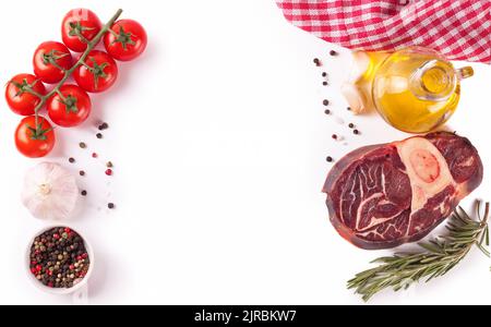 Zutaten zum Kochen. Rohes Rindersteak mit Knochen und Gewürzen, Tomaten, Rosmarin, Knoblauch, Olivenöl isoliert auf einem weißen Hintergrund mit Copy Space in Stockfoto