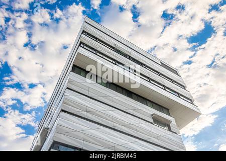 Ein perspektivischer Blick auf ein modernes Gebäude mit überhängenden oberen Stockwerken und einer beeindruckenden Fassade vor einem dramatisch beleuchteten Himmel mit teilweiser Wolkendecke Stockfoto