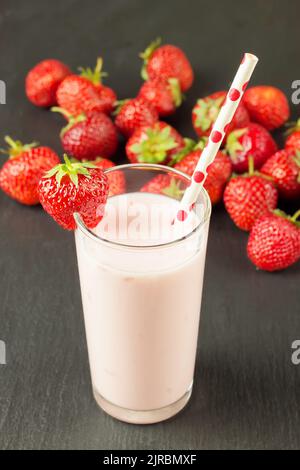 Erdbeerjoghurt im Glas mit einem Strohhalm auf einem schwarzen Schieferbrett trinken Stockfoto