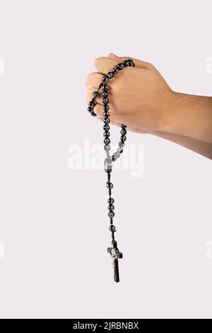 Gefaltete Hände eines jungen Mannes, der einen Rosenkranz während eines Gebetes auf weißem Hintergrund hält Stockfoto