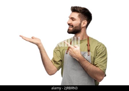 Glücklicher Barkeeper in der Schürze, der etwas Imaginäres hält Stockfoto