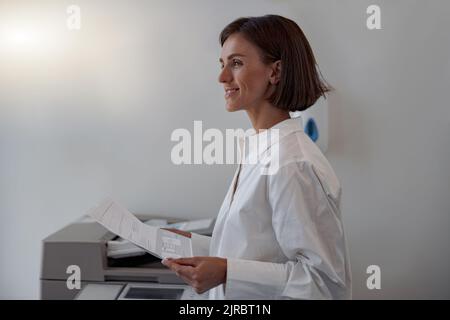 Lächelnde Arbeiterin scannt ein Dokument auf einem Kopiergerät in einem modernen Büro Stockfoto