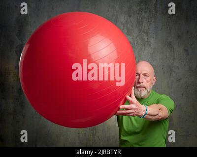 Senior man (Ende 60s) trainiert mit einem großen Schweizer Ball, Aktivität und Fitness über 60 Konzept Stockfoto