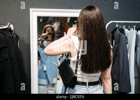 Aus zweiter Hand. Nachhaltige Mode. Junge Latina-Frau kauft gebrauchte nachhaltige Kleidung aus dem Second Hand Charity Shop Stockfoto