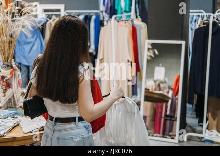 Aus zweiter Hand. Nachhaltige Mode. Junge Latina-Frau kauft gebrauchte nachhaltige Kleidung aus dem Second Hand Charity Shop Stockfoto