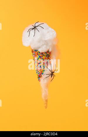Minimales kreatives Konzept aus Eiskegel mit Streuseln, Spinnennetz und Spinnen auf orangefarbenem Hintergrund. Gruseliges und gruseliges Halloween-Konzept. Abs Stockfoto