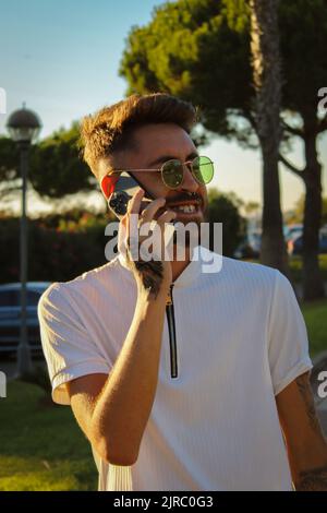 Nahaufnahme eines Mannes in einem weißen Hemd, der draußen am Telefon telefoniert Stockfoto