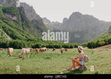 Reise-, Lifestyle-Konzept. Schöne Frau genießt Aussicht auf das Alpendorf in den Alpen. Junge Frau sitzt und entspannt auf den Berghügelchen Stockfoto