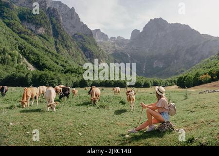 Reise-, Lifestyle-Konzept. Schöne Frau genießt Aussicht auf das Alpendorf in den Alpen. Junge Frau sitzt und entspannt auf den Berghügelchen Stockfoto