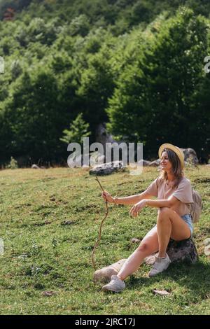 Reise-, Lifestyle-Konzept. Schöne Frau genießt Aussicht auf das Alpendorf in den Alpen. Junge Frau sitzt und entspannt auf den Berghügelchen Stockfoto