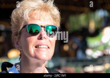 Eine weibliche Besucherin des Disneyland Parks, Paris, Frankreich. Sie blickt auf das Dornröschenschloss, was sich in ihrer Oakley-Sonnenbrille widerspiegelt Stockfoto