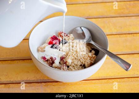 Eine Portion hausgemachter Brombeere und Apfelbrösel in einer Schüssel serviert. Zur traditionellen englischen Fruchtwüste gibt es frische Doppelcreme Stockfoto