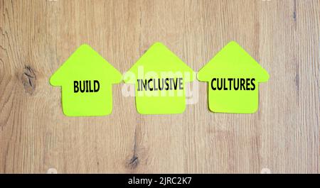 Bauen Sie integrative Kulturen und ein Unterstützungssymbol auf. Konzeptwörter bauen integrative Kulturen auf Grünpapieren auf Wäscheklammern auf. Schöner Holzhintergrund. Busin Stockfoto