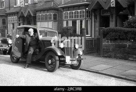 1950s, historisch, ein Gentleman, der die Fahrertür seines Autos öffnete, ein Morris 8 aus der Vorkriegszeit, England, Großbritannien. Die Tür öffnet sich von vorne, auch bekannt als Kutschentür. Stockfoto