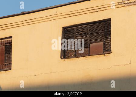 Gelbe Wand einer alten Fabrik mit rostigen Eisenfenstern an den Fenstern. Stockfoto