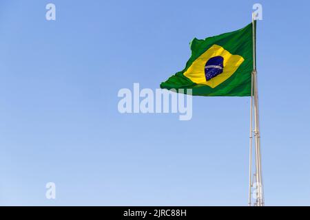 Goiânia, Goias, Brasilien – 23. August 2022: Die Flagge Brasiliens. Die Flagge Brasiliens fliegt, flattert im Wind und der blaue Himmel im Hintergrund. Stockfoto