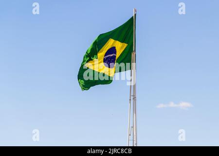 Goiânia, Goias, Brasilien – 23. August 2022: Die Flagge Brasiliens. Die Flagge Brasiliens fliegt, flattert im Wind und der blaue Himmel im Hintergrund. Stockfoto