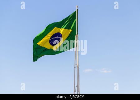 Goiânia, Goias, Brasilien – 23. August 2022: Die Flagge Brasiliens. Die Flagge Brasiliens fliegt, flattert im Wind und der blaue Himmel im Hintergrund. Stockfoto