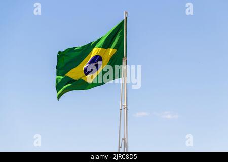Goiânia, Goias, Brasilien – 23. August 2022: Die Flagge Brasiliens. Die Flagge Brasiliens fliegt, flattert im Wind und der blaue Himmel im Hintergrund. Stockfoto