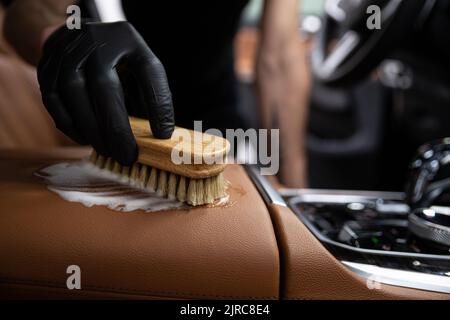 Auto Detaillierung Studio Mitarbeiter reinigt die braune Lederpolsterung eines Autos Stockfoto
