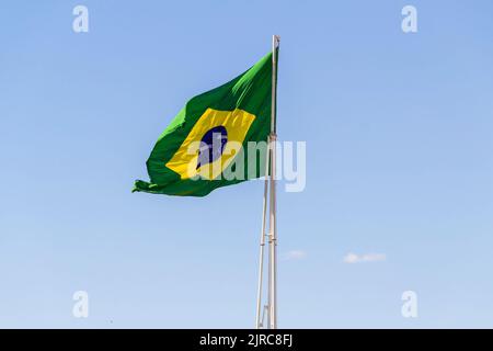 Goiânia, Goias, Brasilien – 23. August 2022: Die Flagge Brasiliens. Die Flagge Brasiliens fliegt, flattert im Wind und der blaue Himmel im Hintergrund. Stockfoto